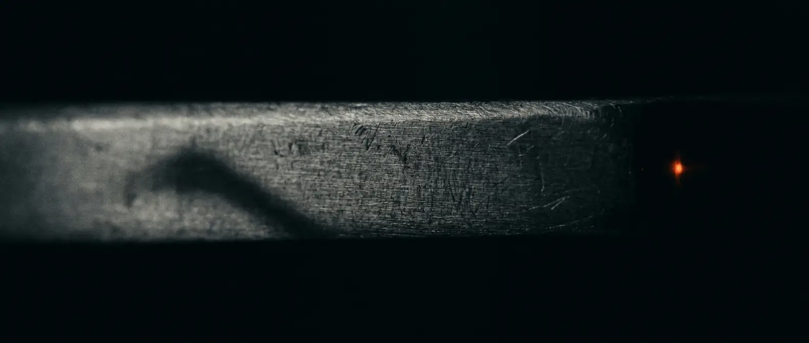 An extreme close-up of finely textured material raked by low light, with a single faint orange glint at the edge.
